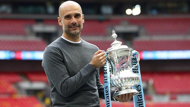 Guardiola, posing with one of his four titles with the Manchester City this year